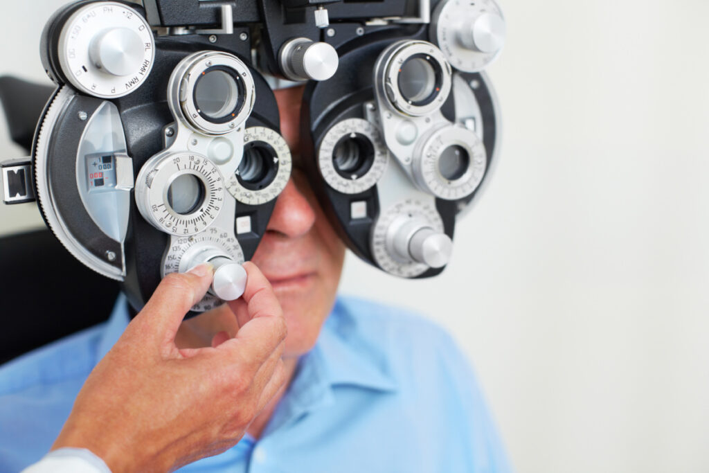 A senior man looking through a phoropter as the ophthalmologist adjusts the lens